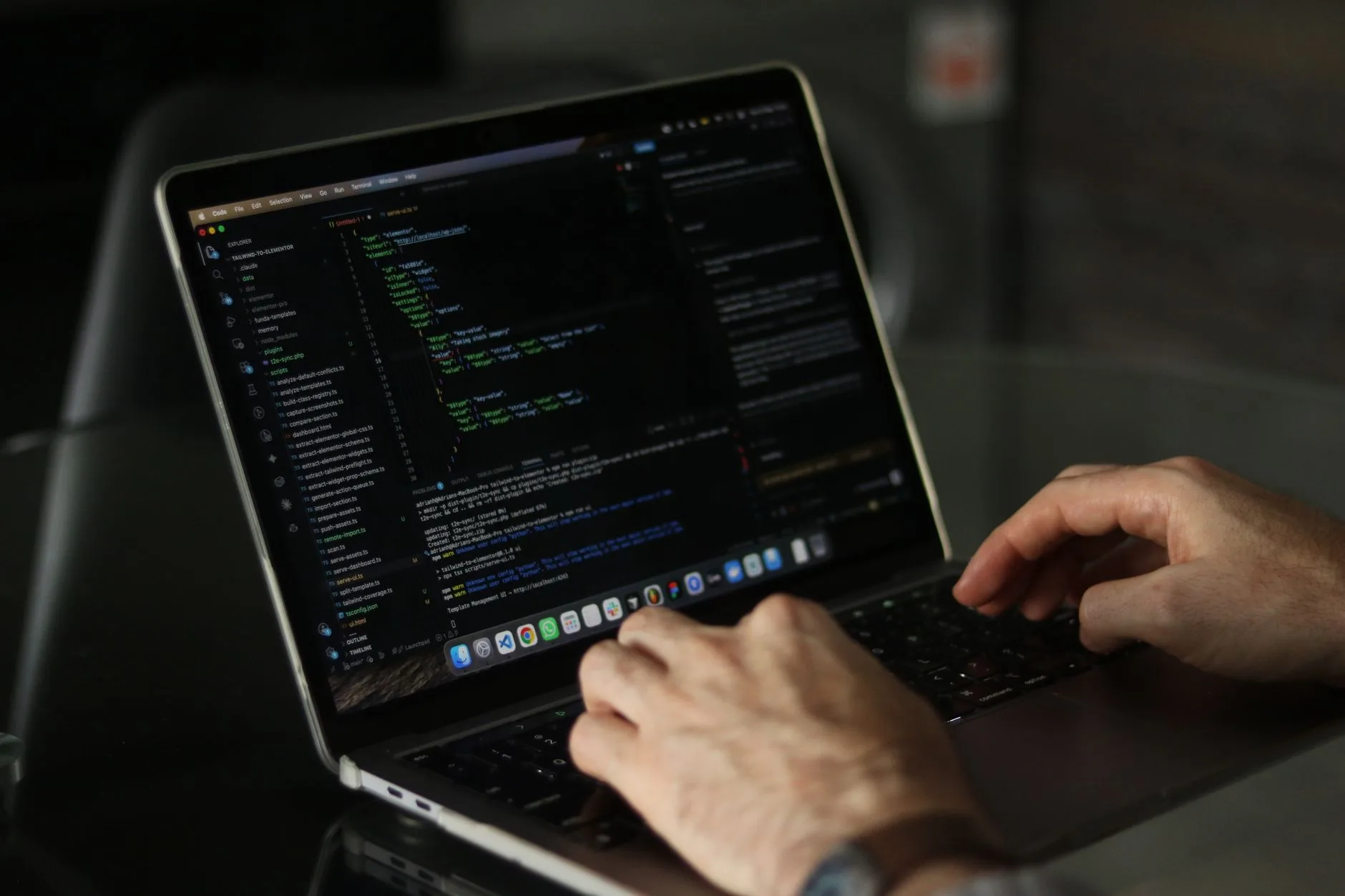 A developer typing on a laptop with code on the screen